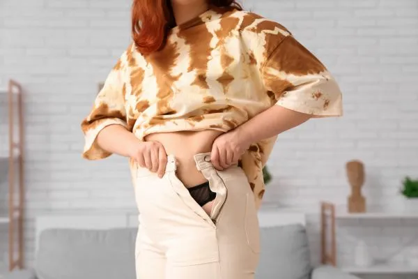 Image of woman trying to do her trousers up after pregnancy weight gain Ledbury